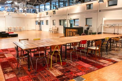 Espace intérieur lumineux avec plantes, tables et chaises, sol en béton et grandes baies vitrées.