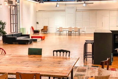 Espace intérieur lumineux avec plantes, tables et chaises, sol en béton et grandes baies vitrées.