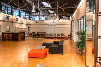 Espace intérieur lumineux avec plantes, tables et chaises, sol en béton et grandes baies vitrées.