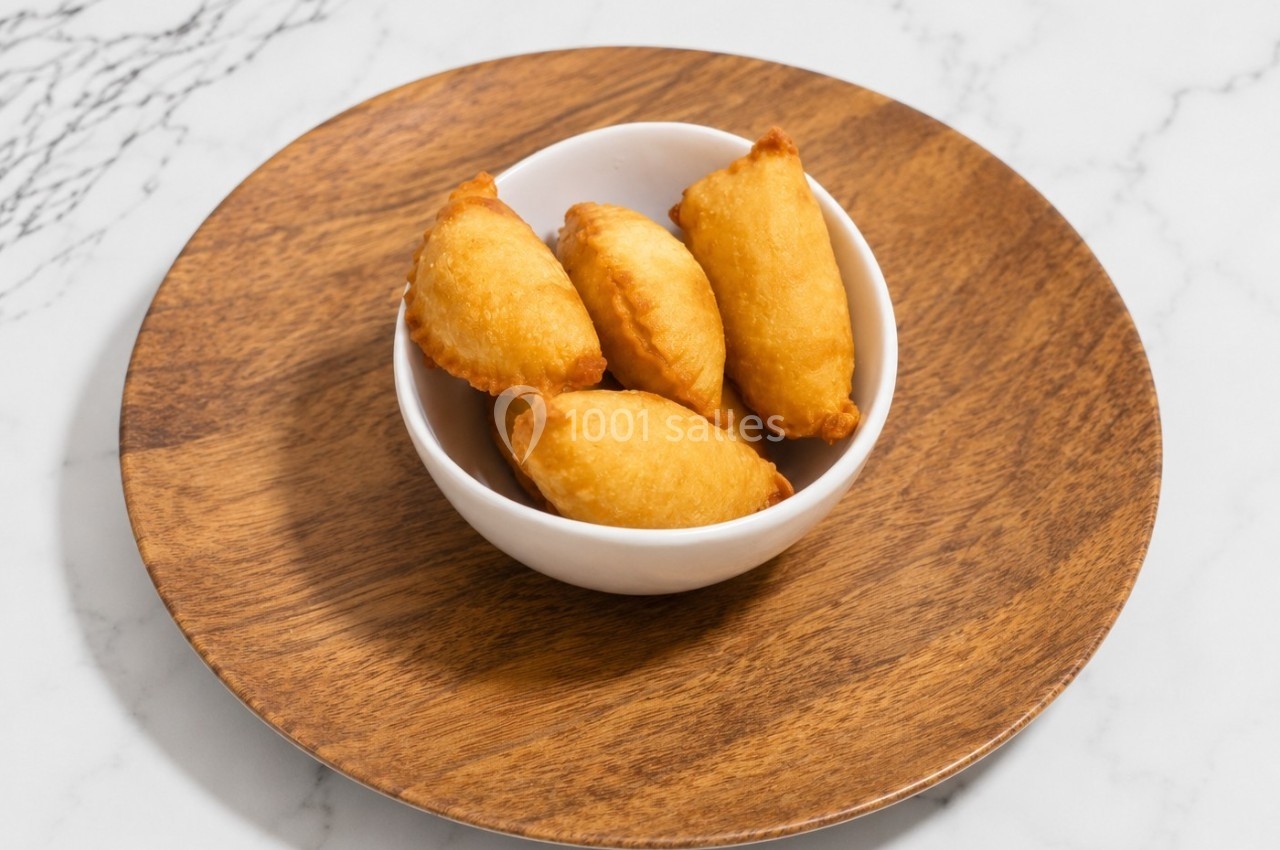 Assiette en bois contenant un bol blanc rempli de petits beignets dorés sur une table en marbre.