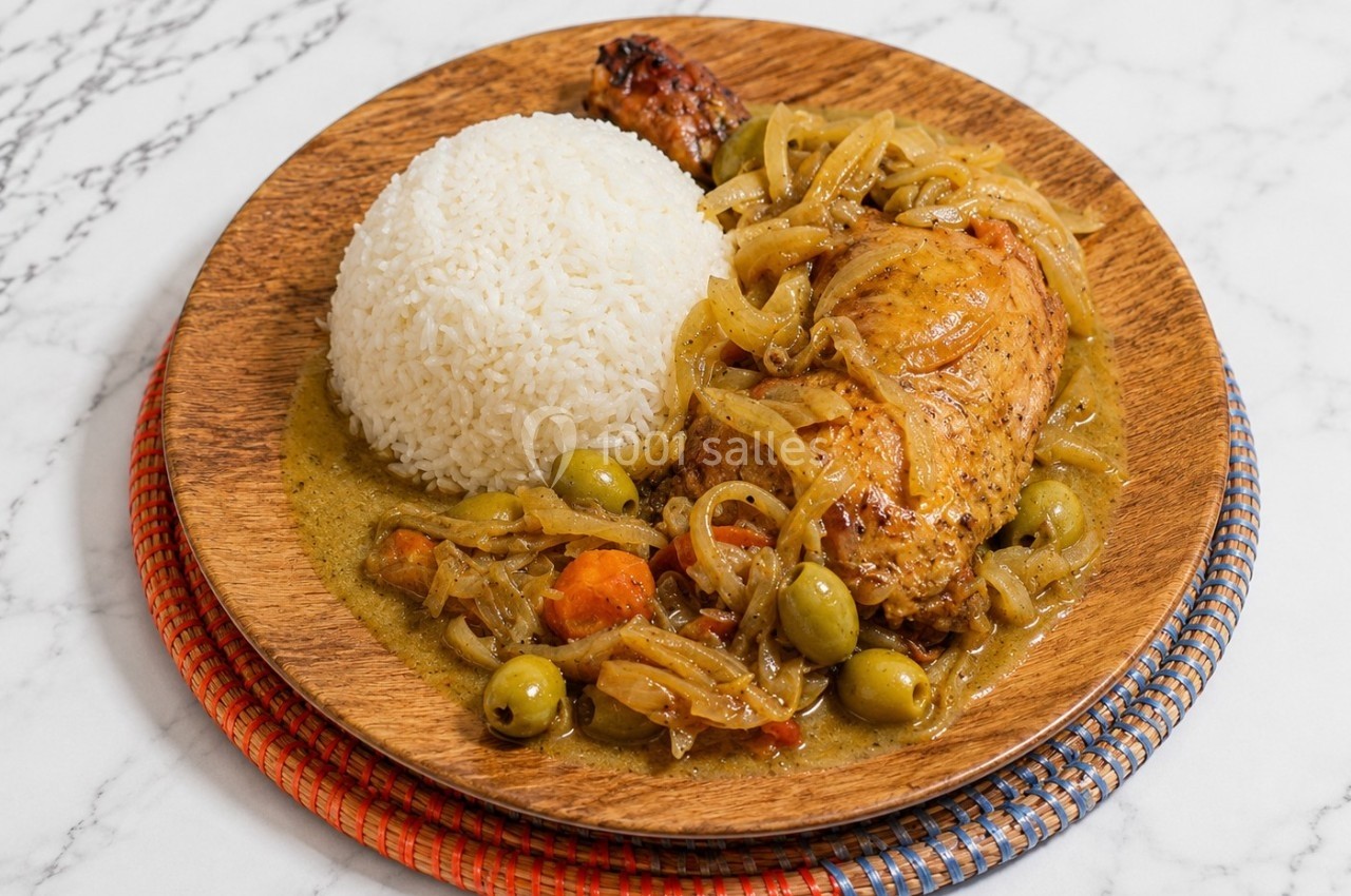 Assiette en bois contenant du riz blanc et un plat mijoté de poulet aux olives, oignons et légumes.