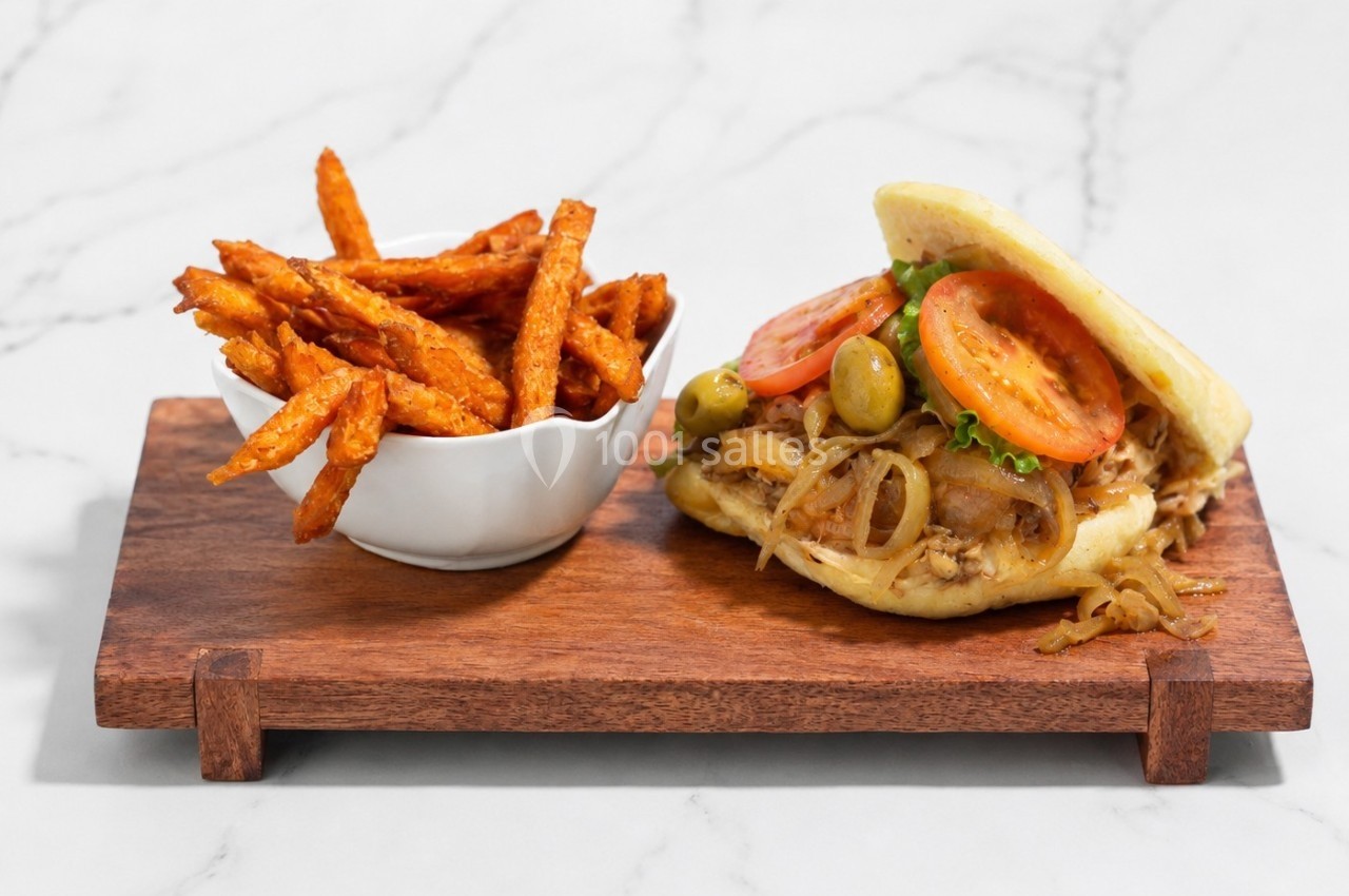 Sandwich garni de poulet, tomates, olives et oignons, accompagné de frites de patate douce sur une planche en bois.