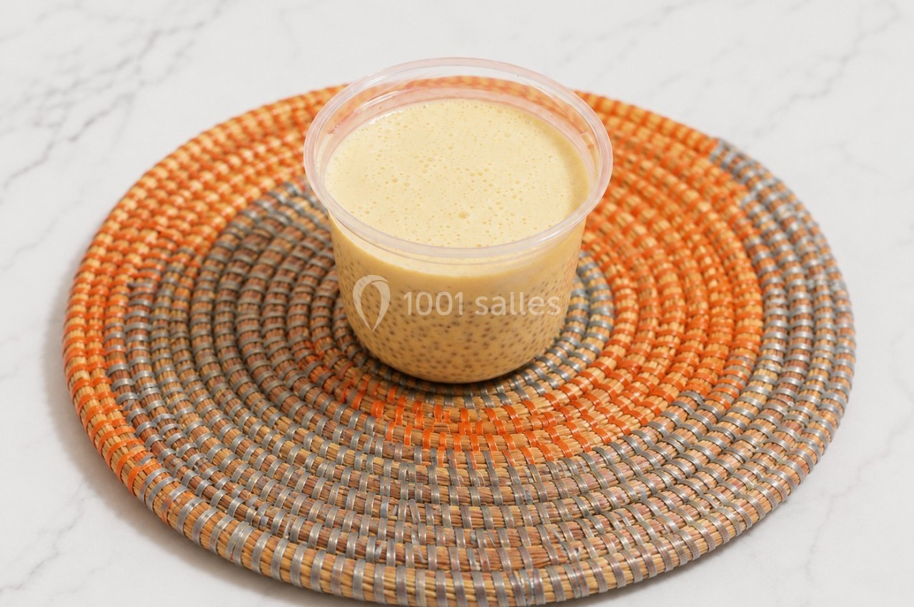 Un pot de pudding au chia et lait, posé sur un dessous de plat tressé orange et gris, sur une table en marbre.