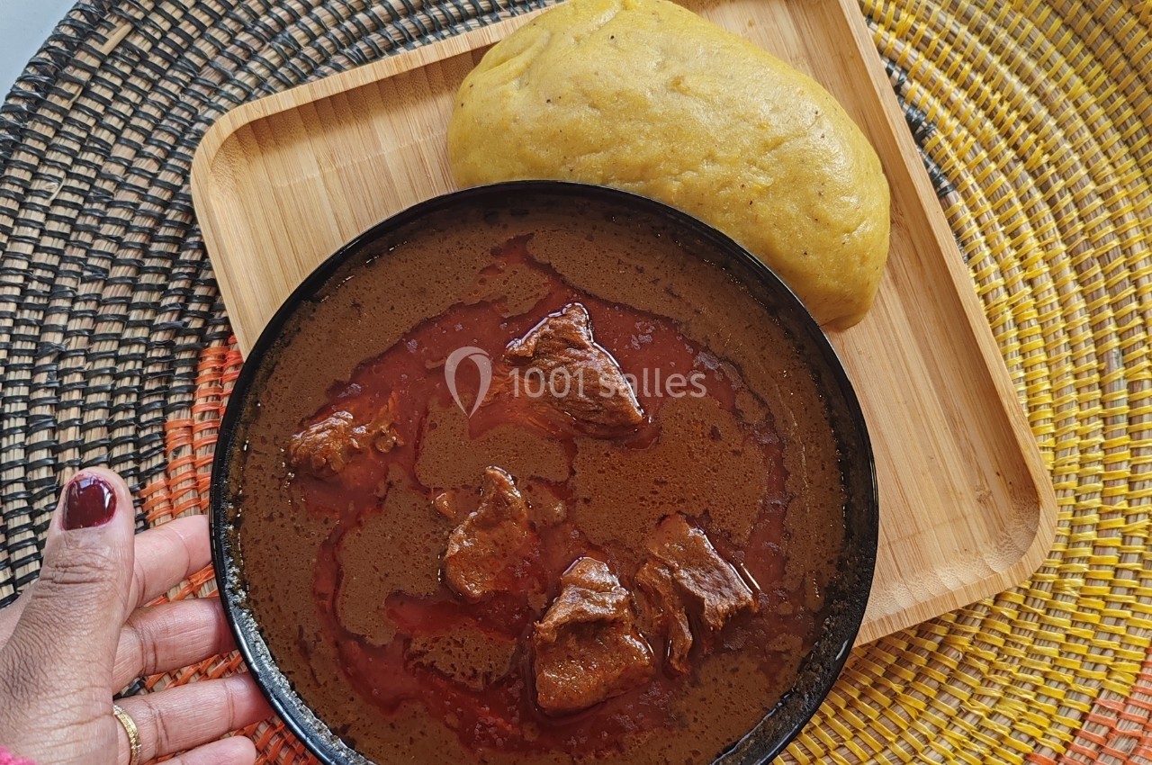Assiette de soupe rouge avec morceaux de viande, accompagnée d'une boule de pâte jaune sur un plateau en bois.