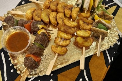 Plateau doré avec brochettes de viande, légumes, morceaux de poulet et plantains frits, accompagné d'une sauce.