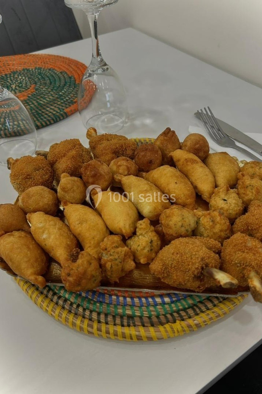 Assortiment de beignets et bouchées frites disposés sur un plateau coloré, avec des couverts et verres en arrière-plan.