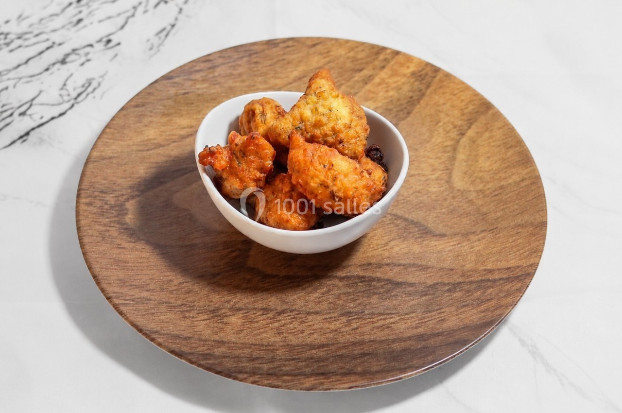 Bol de beignets dorés posés sur une assiette en bois, sur une table en marbre blanc.