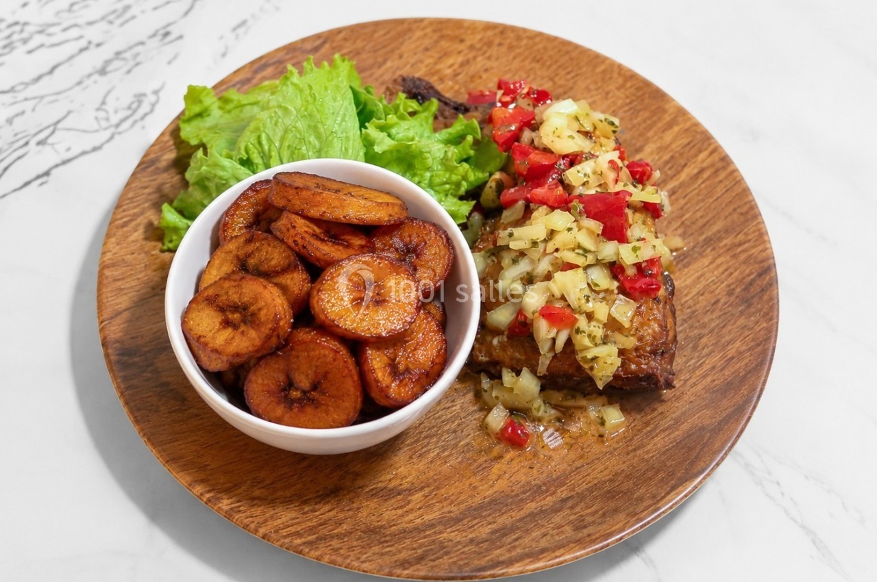 Assiette en bois contenant des bananes plantains frites, une salade verte et une viande garnie de légumes hachés.