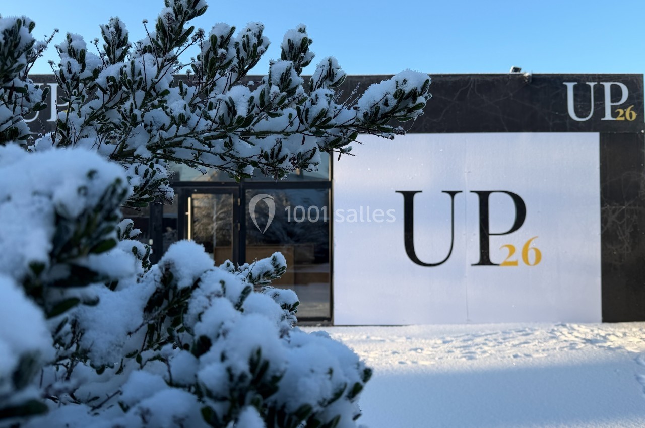 Façade d'un bâtiment noir et blanc marqué ’UP26’, avec des branches enneigées au premier plan.