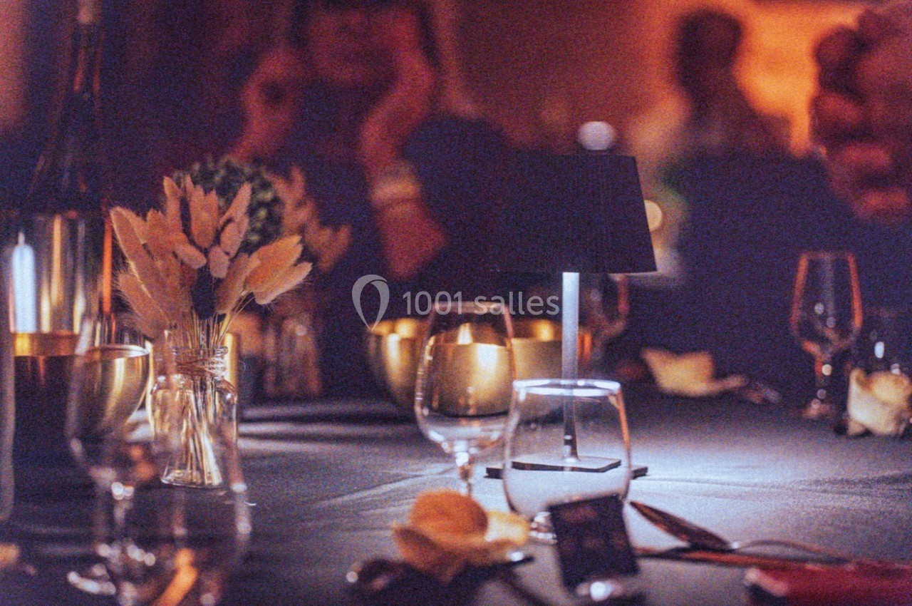 Table élégamment dressée avec verres, bougies et bouquet de fleurs séchées dans une ambiance tamisée.