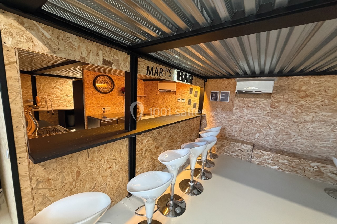 Bar en bois avec comptoir noir, tabourets blancs alignés et décoration intérieure en panneaux OSB.