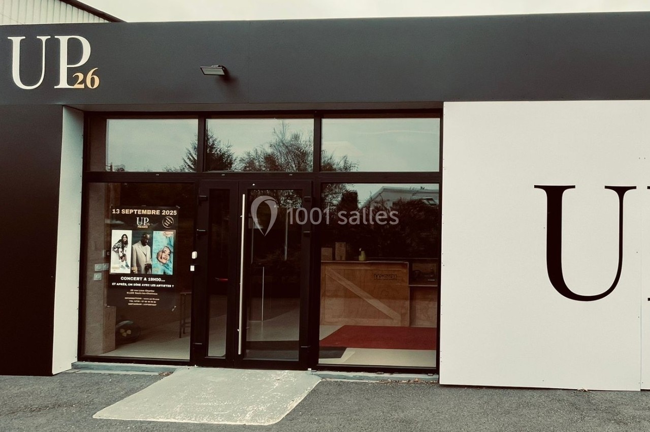 Façade d'un bâtiment avec une entrée vitrée, affiches promotionnelles sur la porte et enseigne ’UP26’ visible.