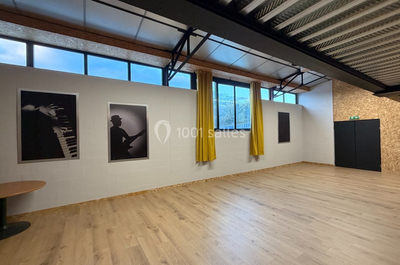 Salle lumineuse avec parquet, murs blancs décorés de photos d'instruments, grandes fenêtres et rideaux jaunes.