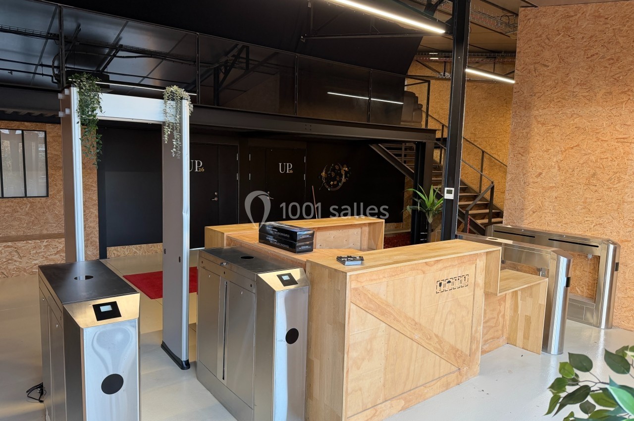 Vue d'un espace d'accueil moderne avec tourniquets en métal, comptoir en bois et décoration minimaliste.