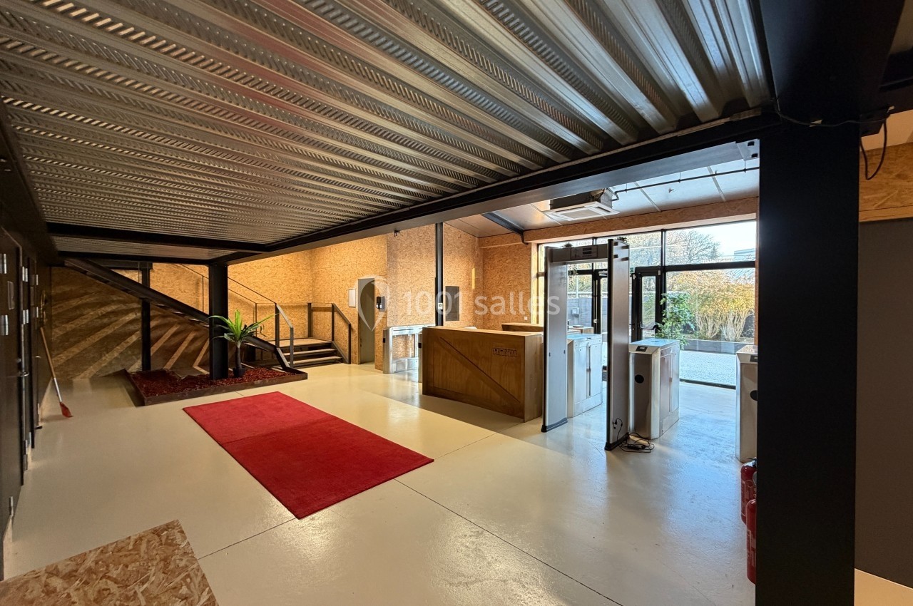 Entrée d'un espace moderne avec escalier, comptoir d'accueil en bois, tapis rouge et lumière naturelle.