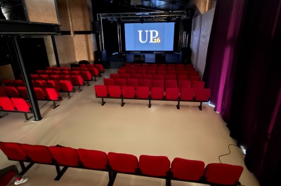 Salle de spectacle avec scène éclairée, artistes en représentation et public assis dans des fauteuils rouges.