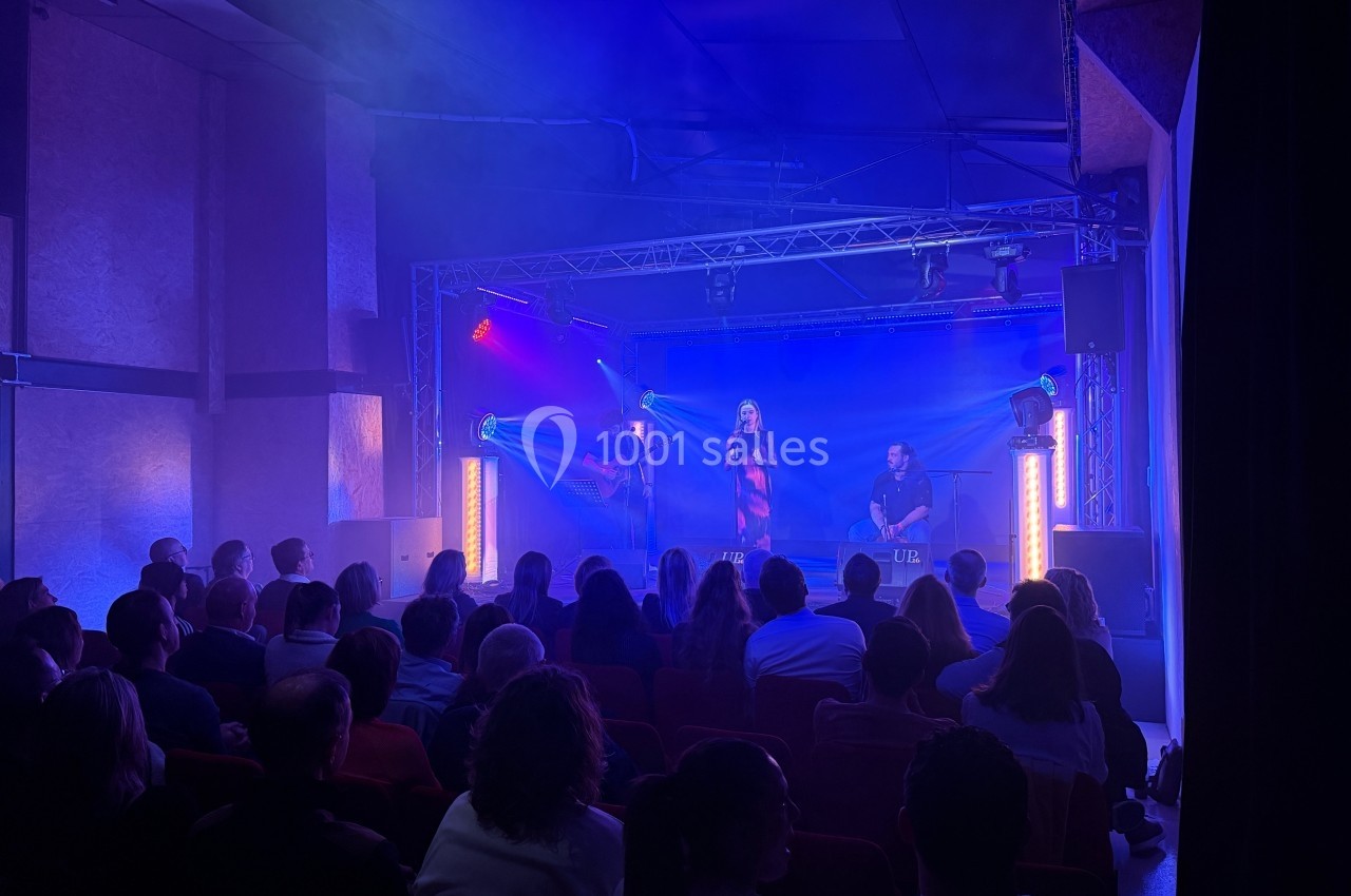 Un groupe de musiciens se produit sur scène dans une salle sombre, éclairée par des lumières bleues et violettes.