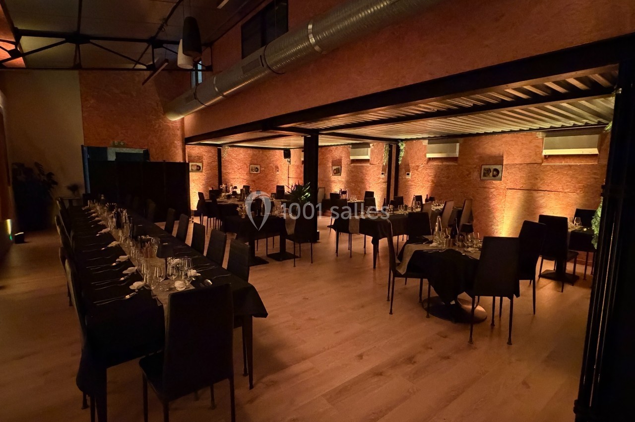 Salle de réception chaleureuse avec tables dressées, éclairage tamisé et murs en briques apparentes.