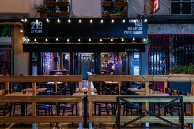 Bouteilles de vin variées alignées sur un comptoir en bois, avec un fond de bar décoré et éclairé.