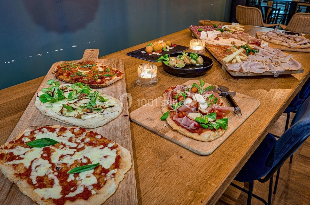 Plateau de pizzas variées et planches de charcuterie et fromages disposés sur une table en bois avec des bougies.