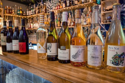 Bouteilles de vin variées alignées sur un comptoir en bois, avec un fond de bar décoré et éclairé.