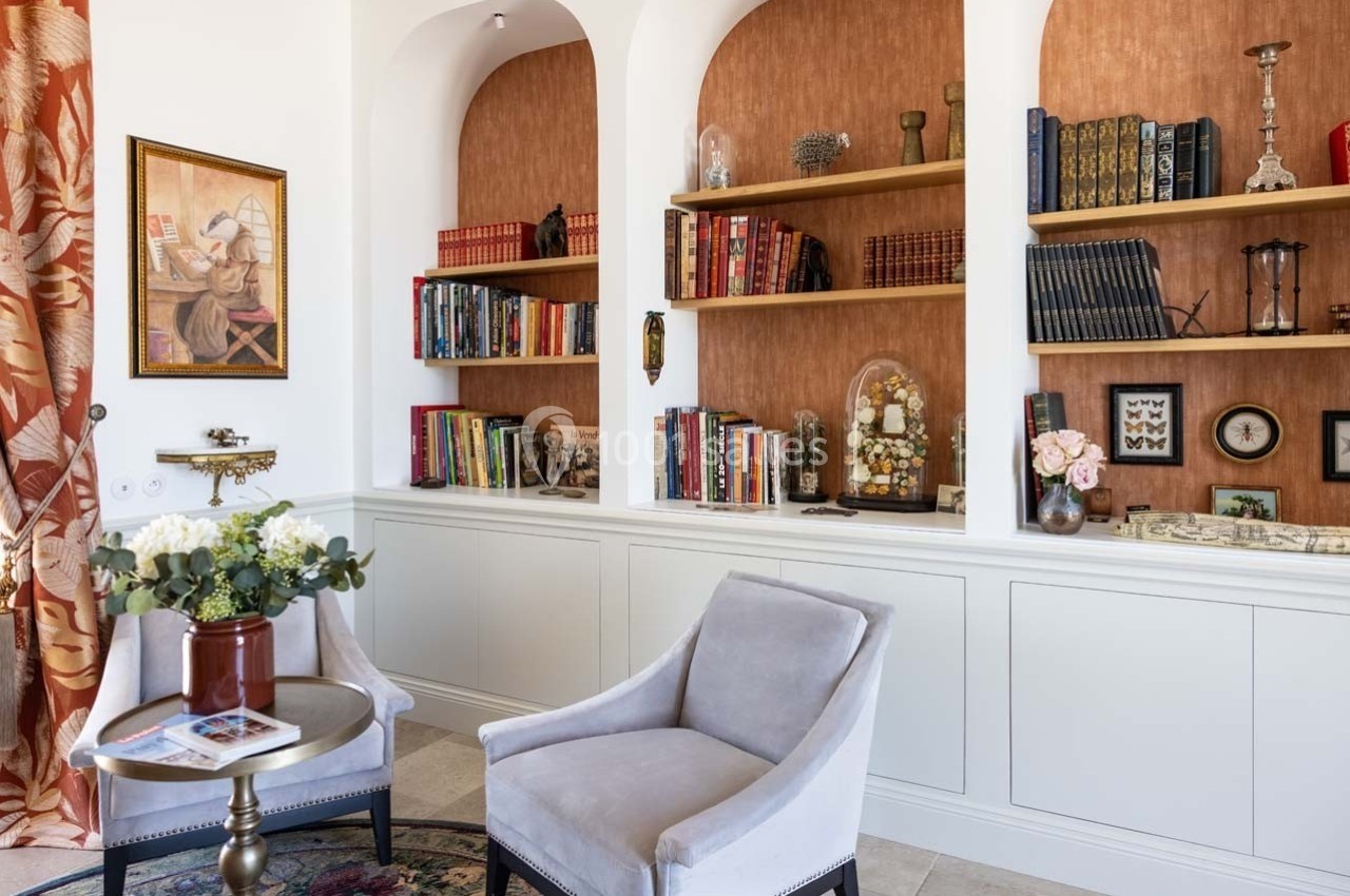 Deux fauteuils devant une bibliothèque intégrée avec étagères remplies de livres et objets décoratifs.