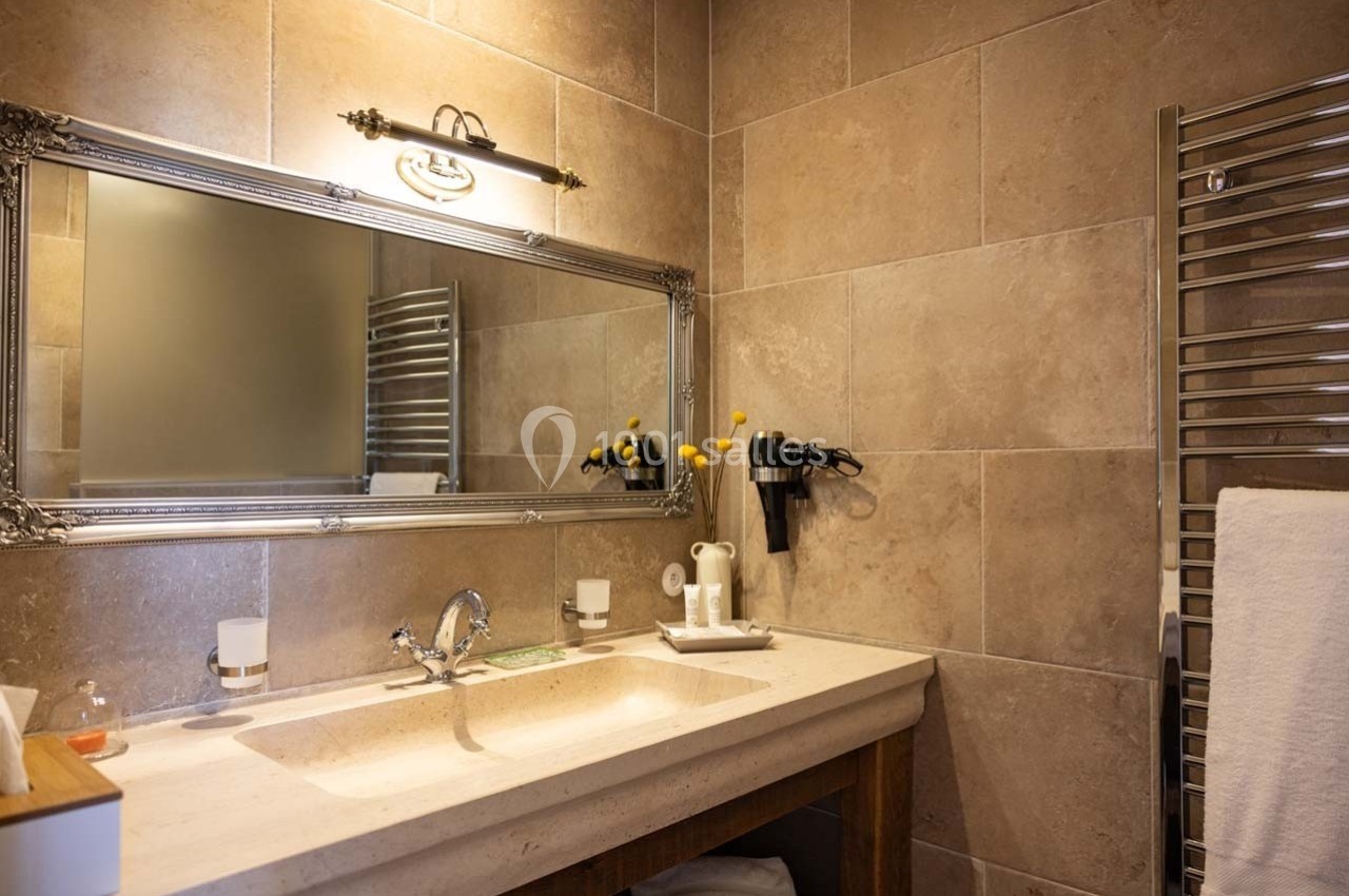 Salle de bain avec un lavabo, un grand miroir, un porte-serviettes chauffant et des murs en carrelage beige.