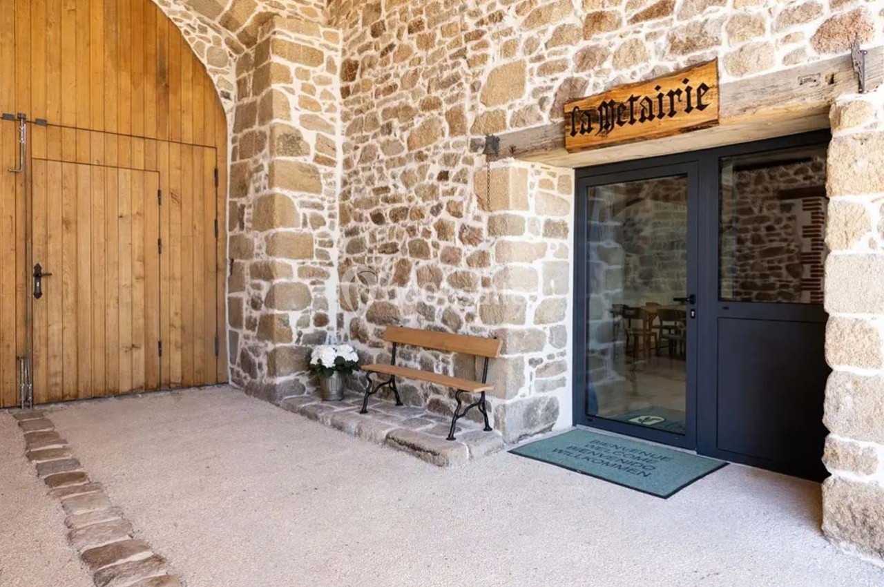 Entrée d'un bâtiment en pierre avec une porte vitrée, une enseigne ’La Métairie’ et un banc en bois à côté.