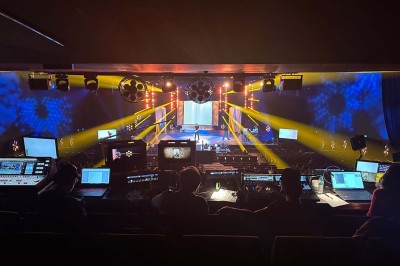 Scène éclairée avec instruments de musique, tabourets et écran affichant un logo ’ESB’ sur un fond de briques.