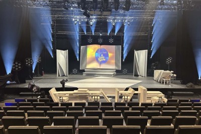 Scène éclairée avec instruments de musique, tabourets et écran affichant un logo ’ESB’ sur un fond de briques.