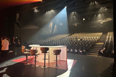 Scène éclairée avec instruments de musique, tabourets et écran affichant un logo ’ESB’ sur un fond de briques.