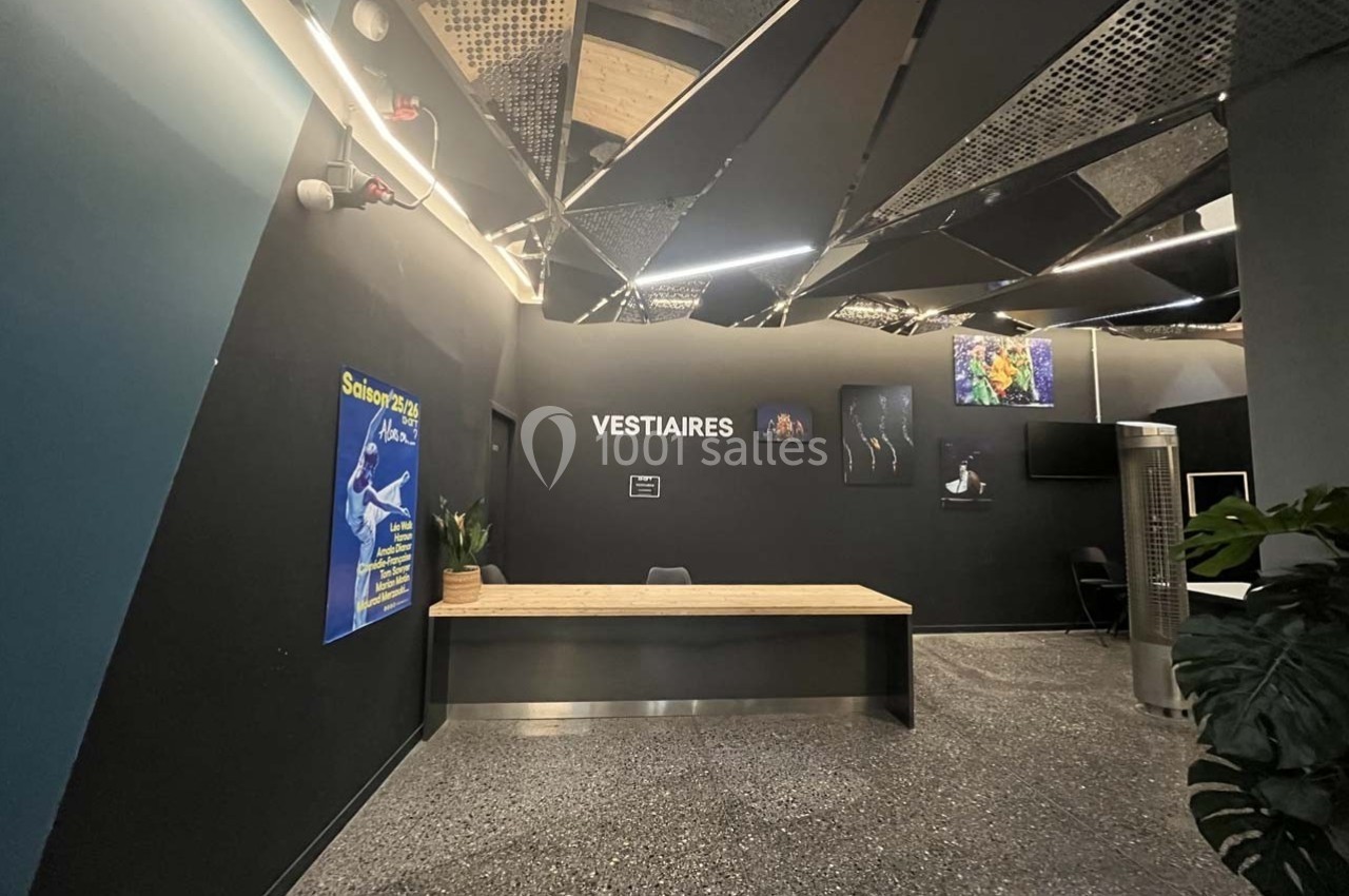 Accueil des vestiaires avec un comptoir en bois, un mur noir, des affiches et un plafond au design moderne.