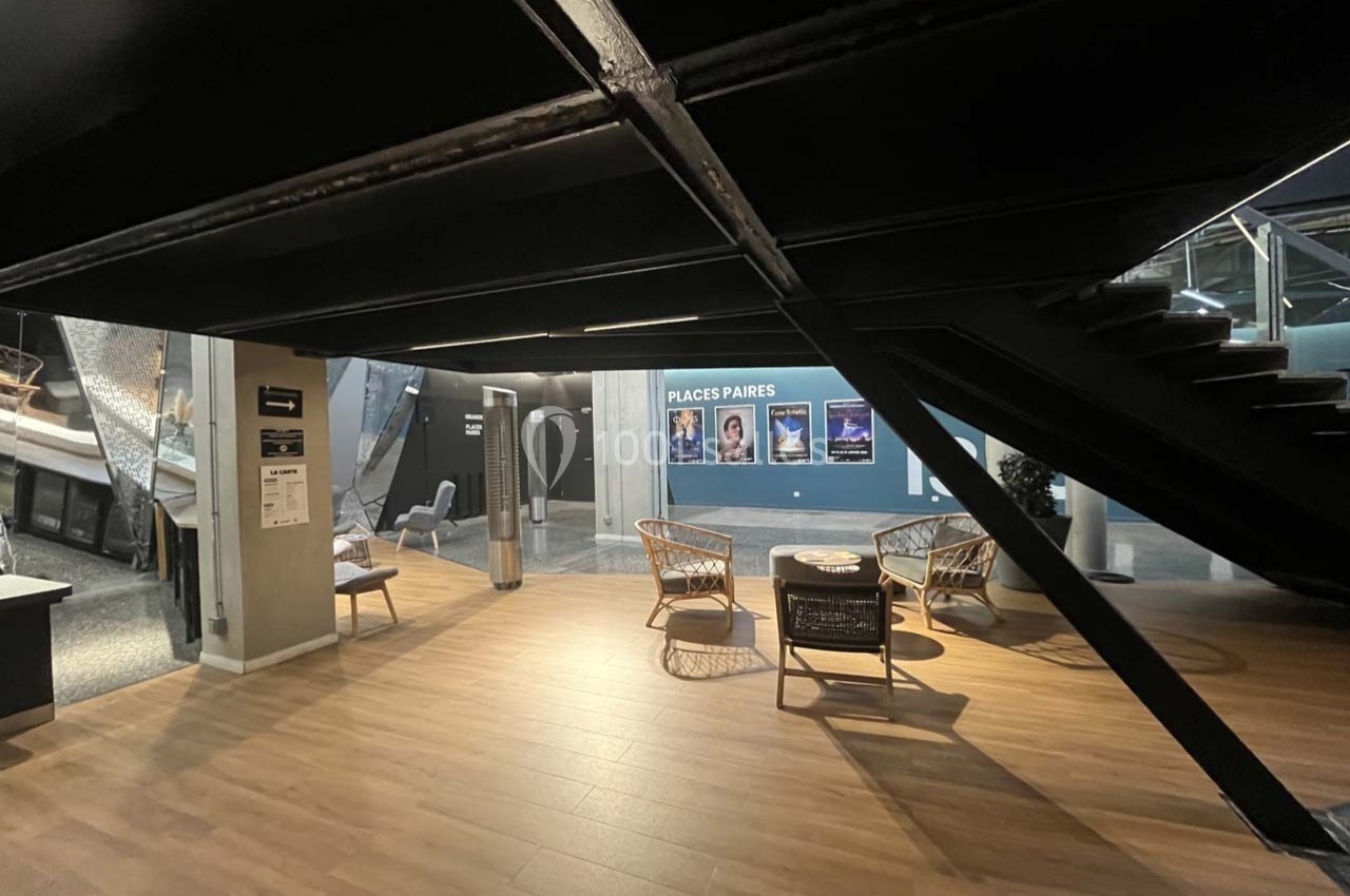 Espace intérieur moderne avec sol en bois, chaises en rotin, affiches murales et escalier métallique noir.