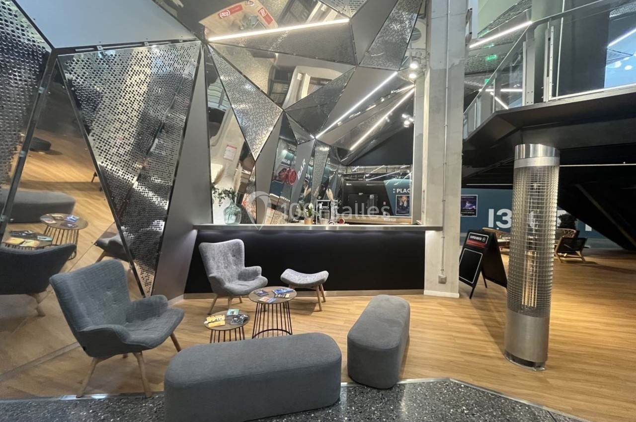 Espace d'accueil moderne avec mobilier gris, tables basses et murs aux surfaces métalliques réfléchissantes.