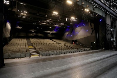 Scène éclairée avec instruments de musique, tabourets et écran affichant un logo ’ESB’ sur un fond de briques.