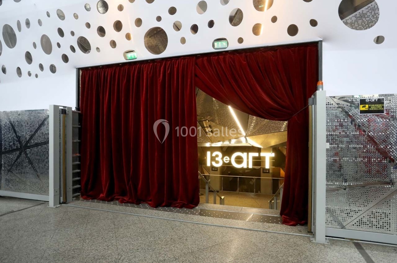 Entrée d'un espace avec des rideaux rouges ouverts, un sol en marbre et des murs métalliques perforés.