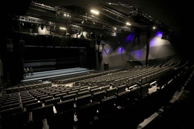 Scène éclairée avec instruments de musique, tabourets et écran affichant un logo ’ESB’ sur un fond de briques.