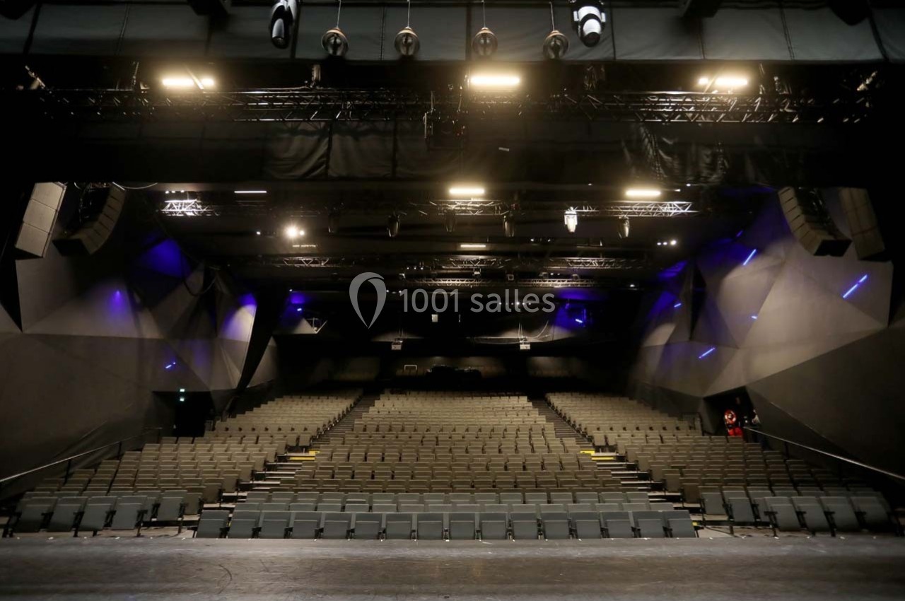 Salle de spectacle vide avec rangées de sièges et éclairage de scène visible depuis la scène.
