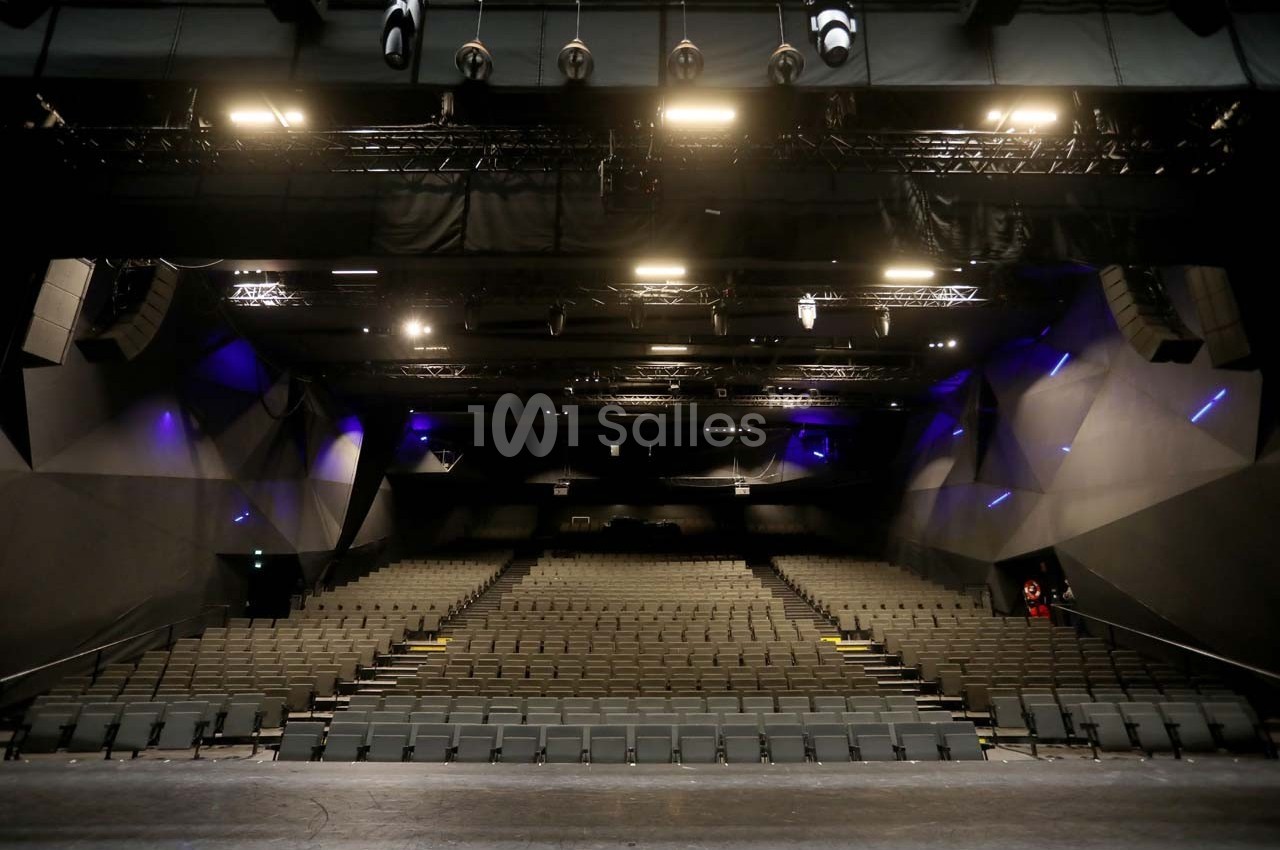 Salle de spectacle vide avec rangées de sièges et éclairage de scène visible depuis la scène.