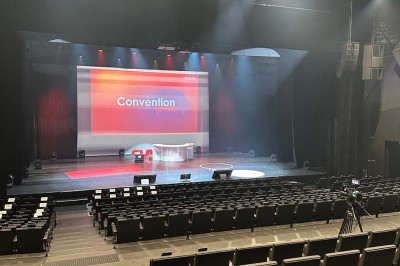 Scène éclairée avec instruments de musique, tabourets et écran affichant un logo ’ESB’ sur un fond de briques.