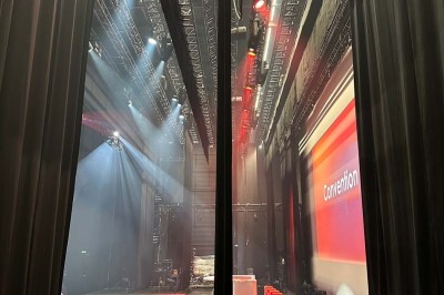 Scène éclairée avec instruments de musique, tabourets et écran affichant un logo ’ESB’ sur un fond de briques.