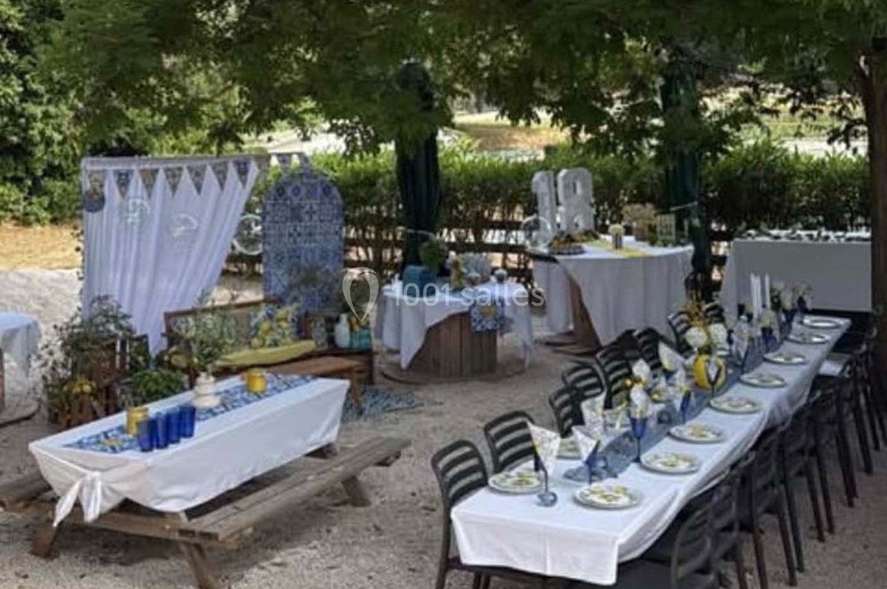 Tables dressées pour un repas en extérieur, décorées avec des motifs bleus et blancs sous des arbres.