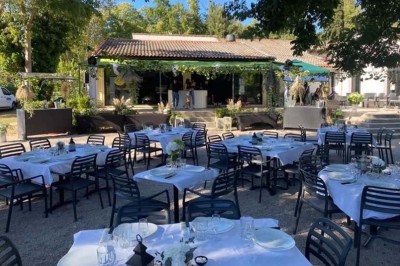 Terrasse animée d'un restaurant en soirée, avec des guirlandes lumineuses et des convives attablés sous un arbre.