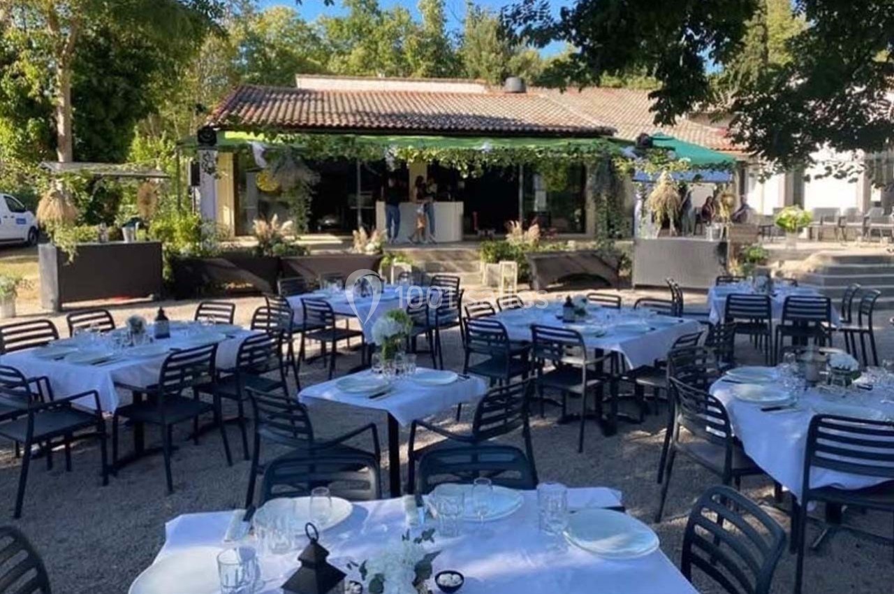 Terrasse extérieure aménagée avec des tables dressées pour un événement, entourée de verdure et d'un bâtiment en arrière…