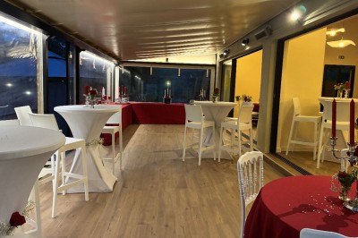 Terrasse animée d'un restaurant en soirée, avec des guirlandes lumineuses et des convives attablés sous un arbre.