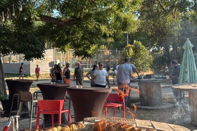Terrasse animée d'un restaurant en soirée, avec des guirlandes lumineuses et des convives attablés sous un arbre.