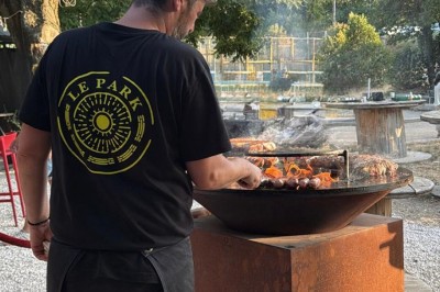 Terrasse animée d'un restaurant en soirée, avec des guirlandes lumineuses et des convives attablés sous un arbre.