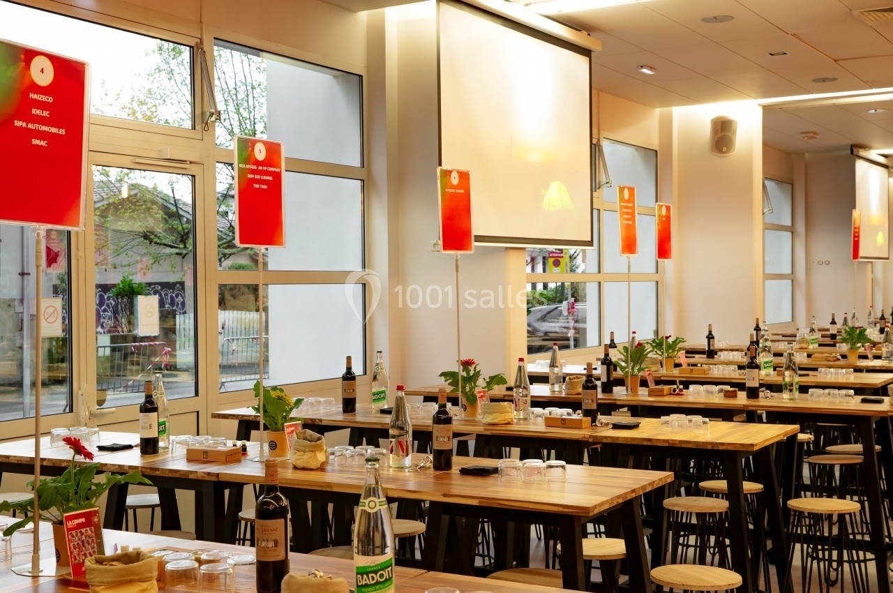 Salle de restauration lumineuse avec tables en bois dressées, bouteilles, verres et décorations simples.