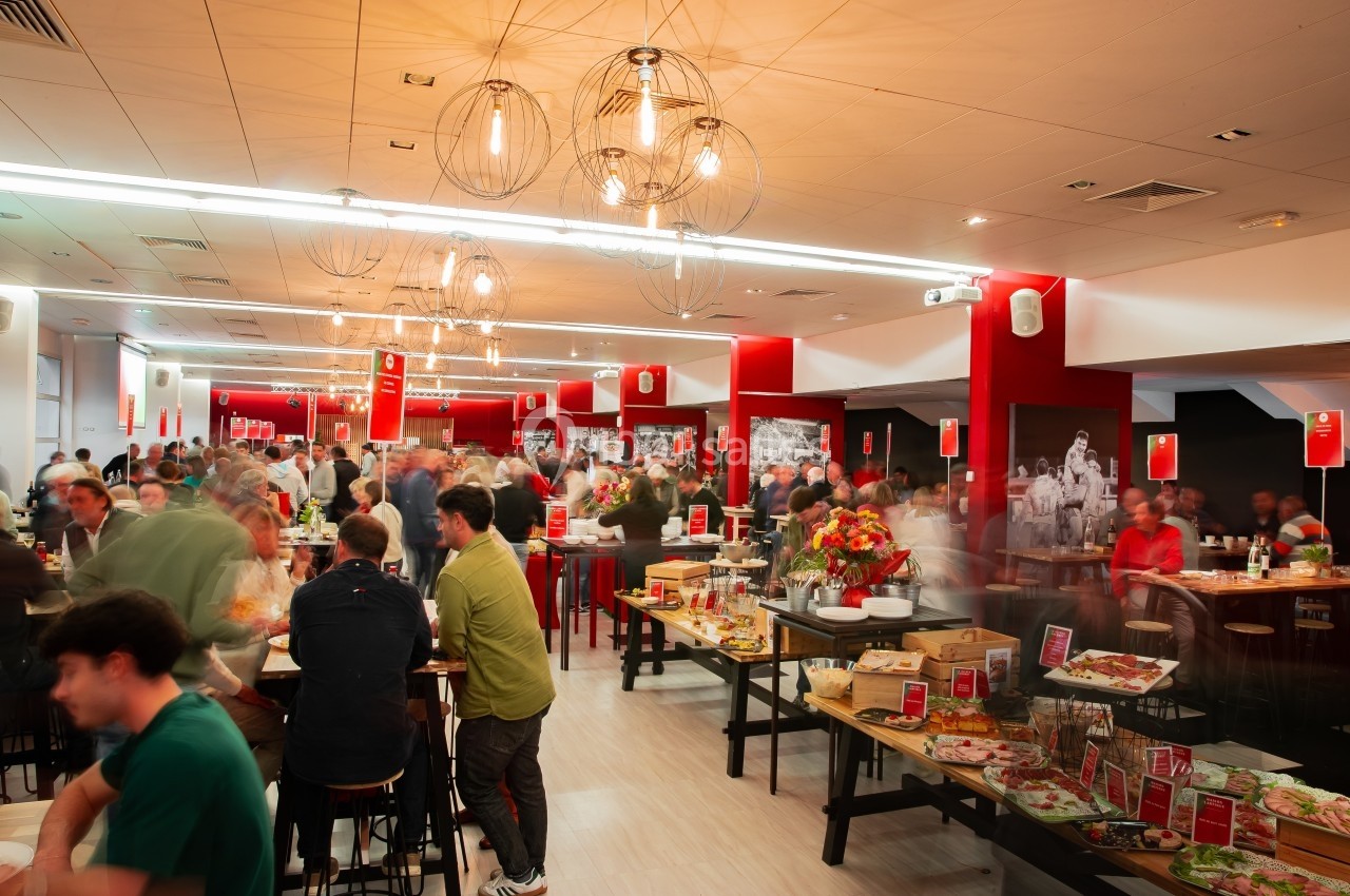 Salle animée avec des tables, des convives et un buffet varié dans un décor moderne aux tons rouges et blancs.
