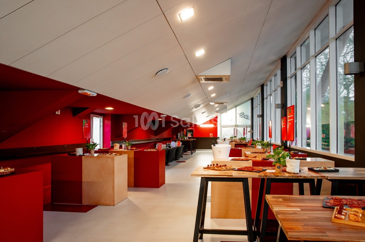 Salle lumineuse avec tables en bois, murs rouges et baies vitrées donnant sur un extérieur arboré.